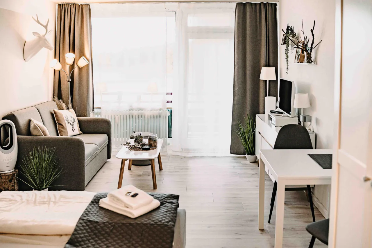 Studio mit Schreibtisch, Sofa und Fensterfront – Haus Vier Jahreszeiten am See Harzflair in Hahnenklee